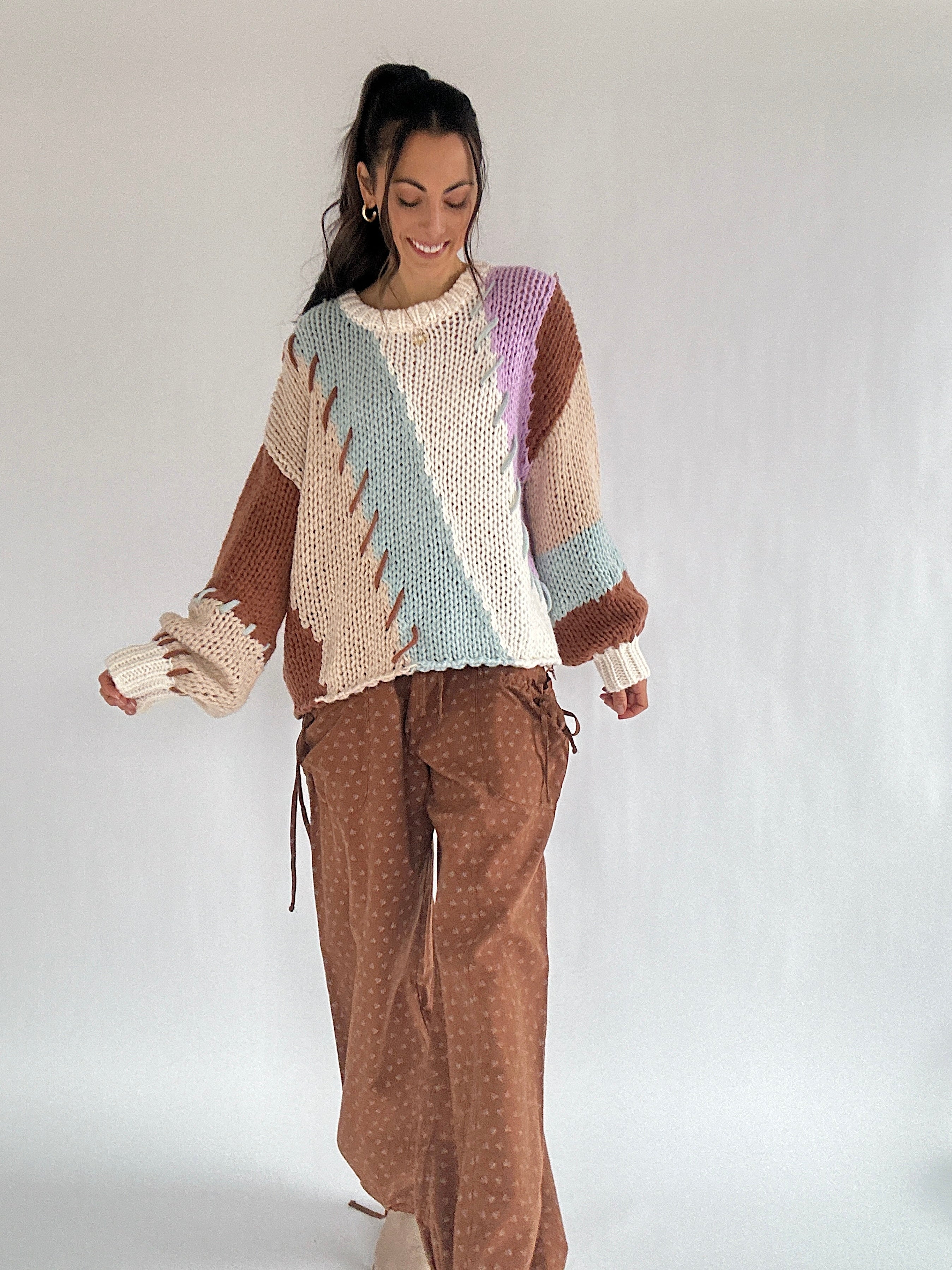 Woman wearing a colorful diagonal striped knit sweater and brown pants on a white background