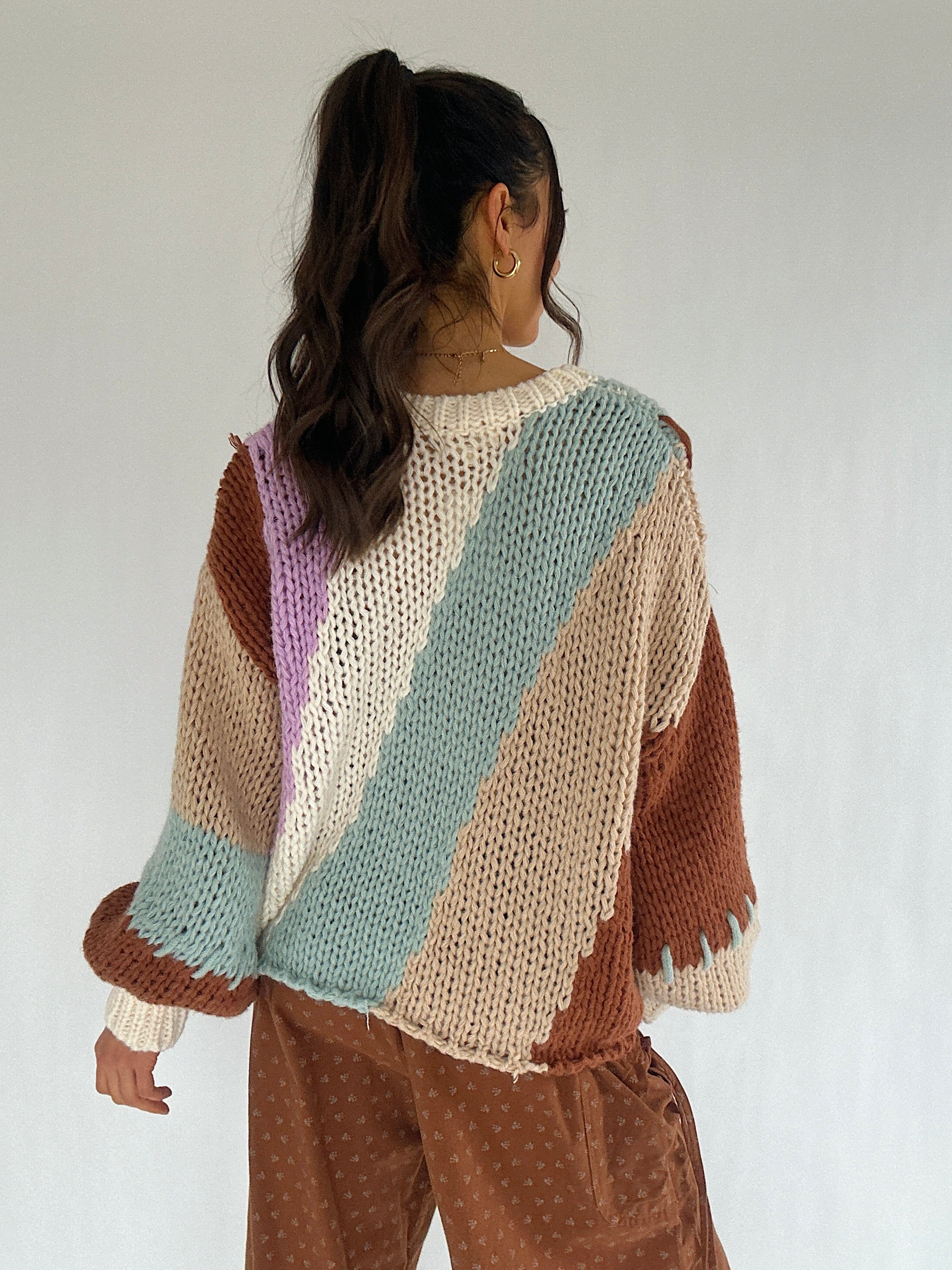 Person wearing a colorful knitted sweater with a neutral background showing the back