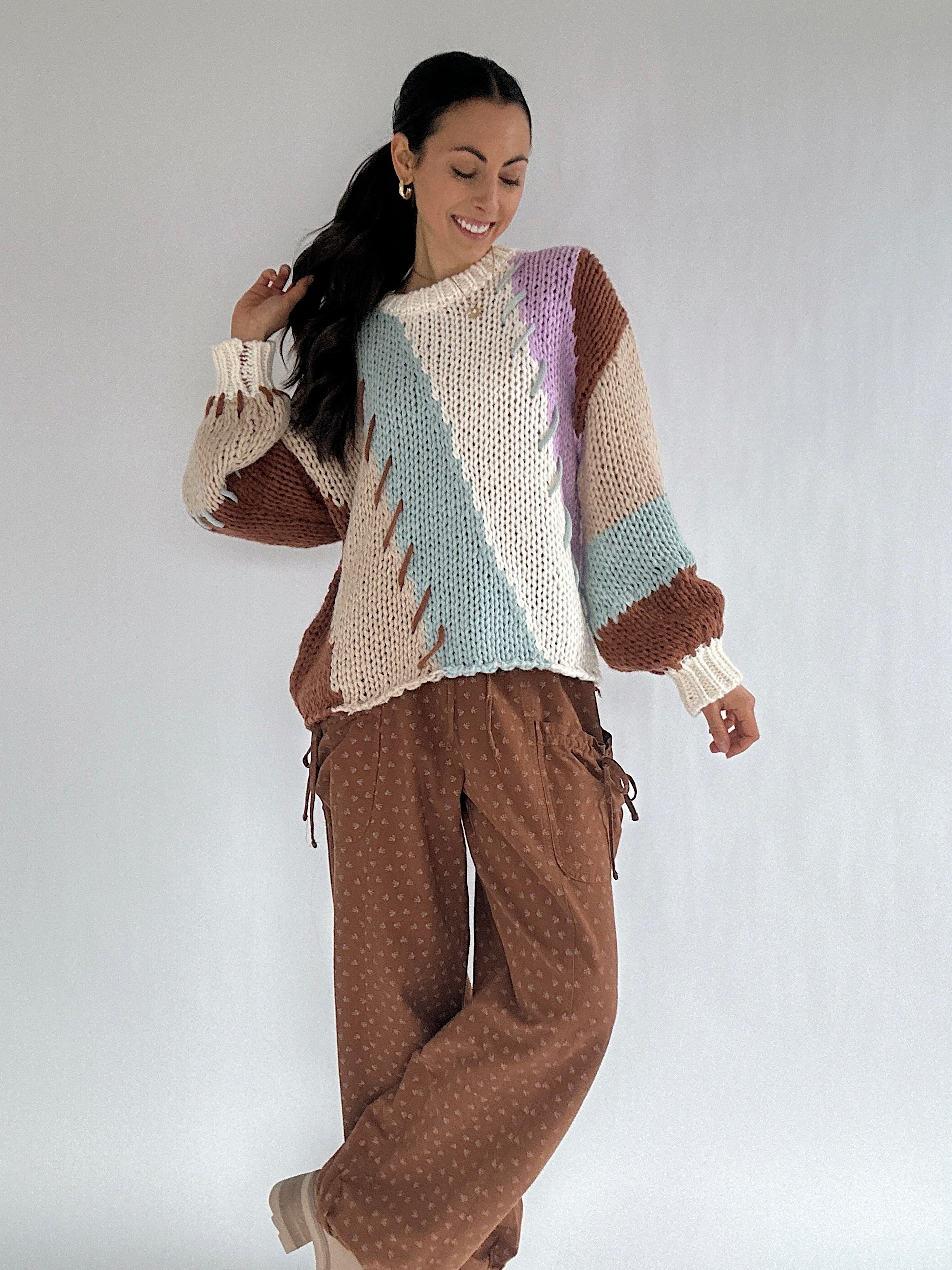 Woman wearing a colorful sweater and brown pants against a white background
