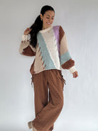 Woman wearing a colorful sweater and brown pants against a white background