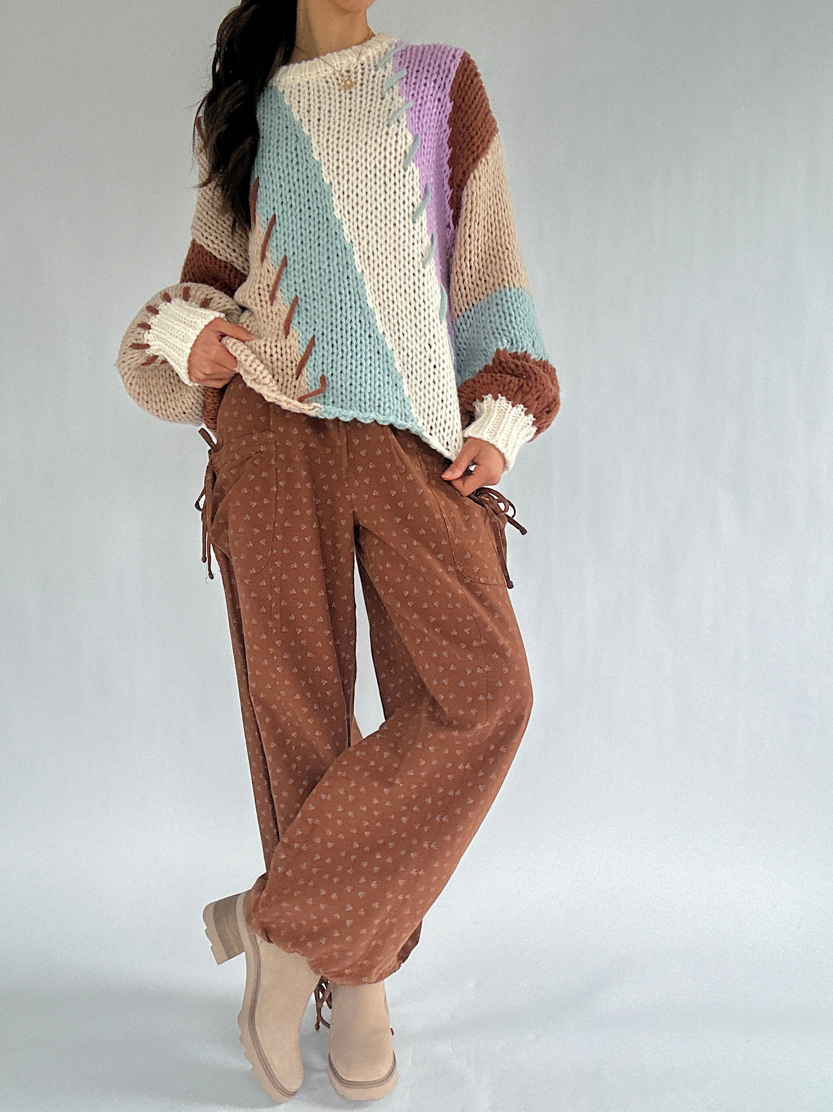 Person wearing a colorful knit sweater and brown pants on a plain background
