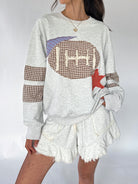 A woman wearing a light heather gray sweatshirt with a brown and white gingham football patch, a purple striped pennant patch, and a red star applique, paired with matching frayed shorts.