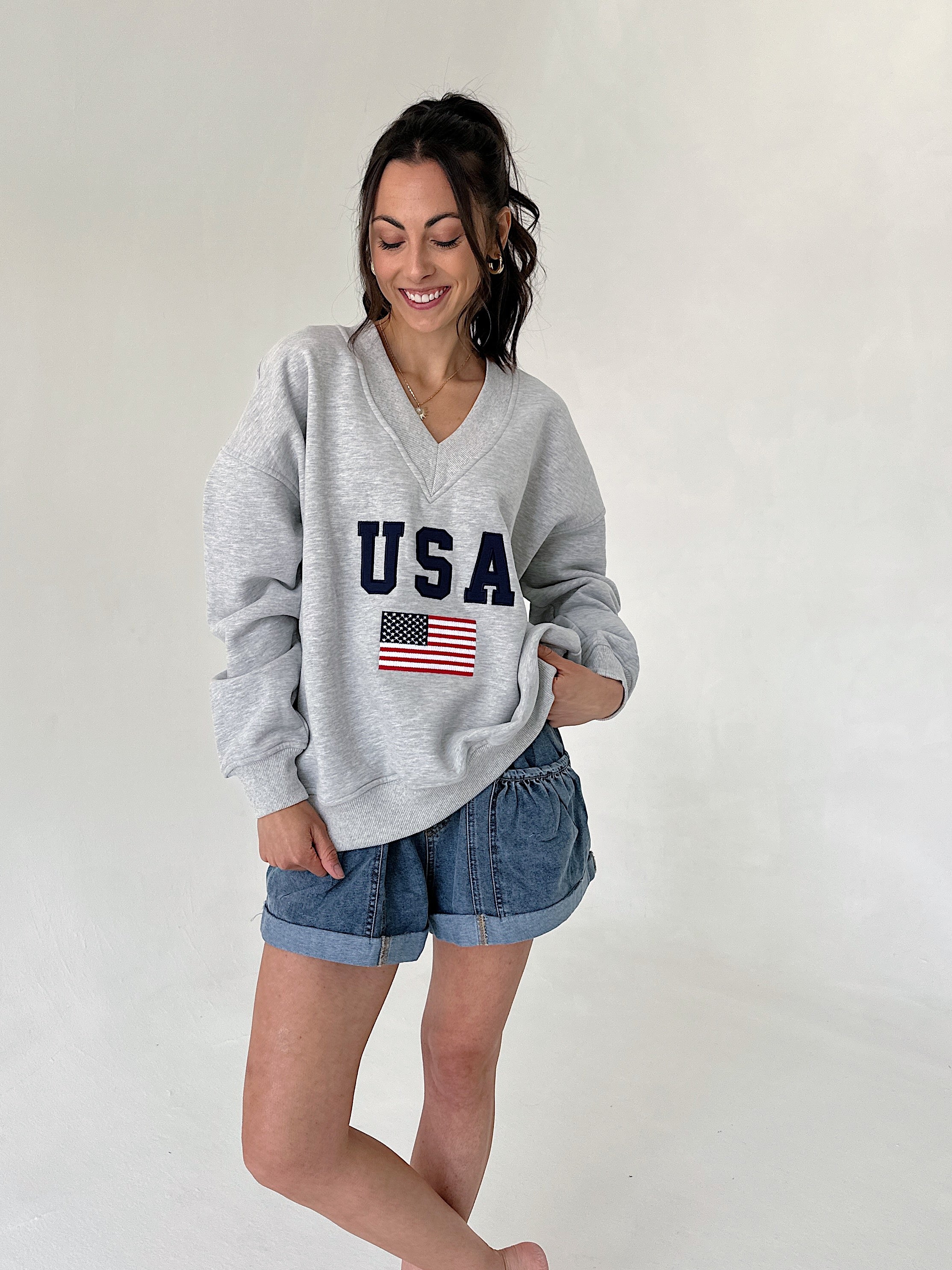 Woman wearing a gray sweatshirt with 'USA' and an American flag design, standing against a plain background.