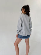 Person wearing a gray sweatshirt and denim shorts against a plain background