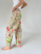 A person wearing beige wide-leg pants with a colorful vegetable print, standing barefoot against a light gray studio background.