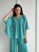 Woman wearing a teal textured outfit with floral crochet patterns against a white background