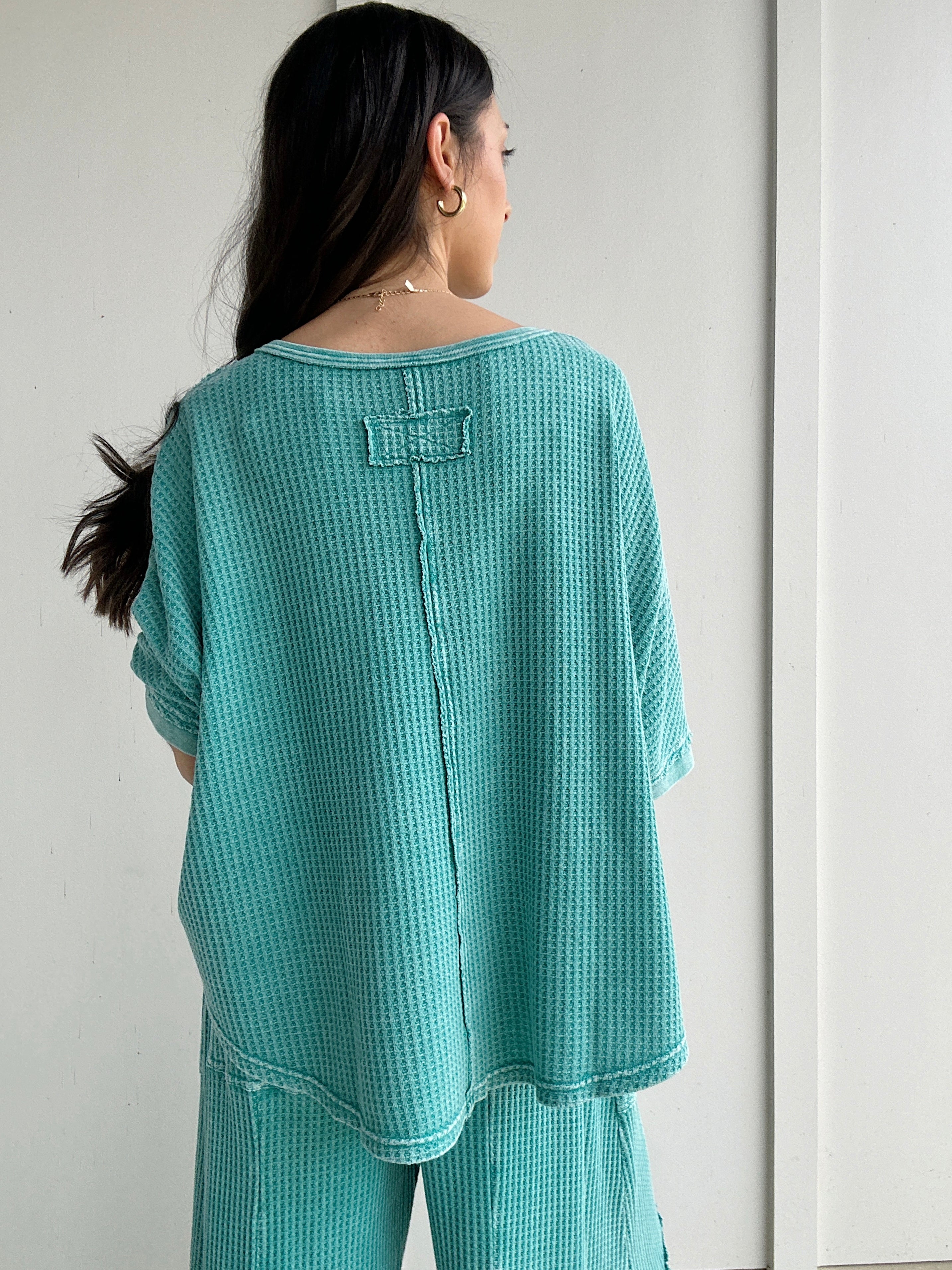 Person wearing a teal textured outfit against a white background showing back