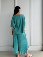 Person wearing a teal outfit standing against a white wall showing back