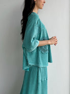 Woman wearing a teal textured outfit with lace details against a plain background showing side
