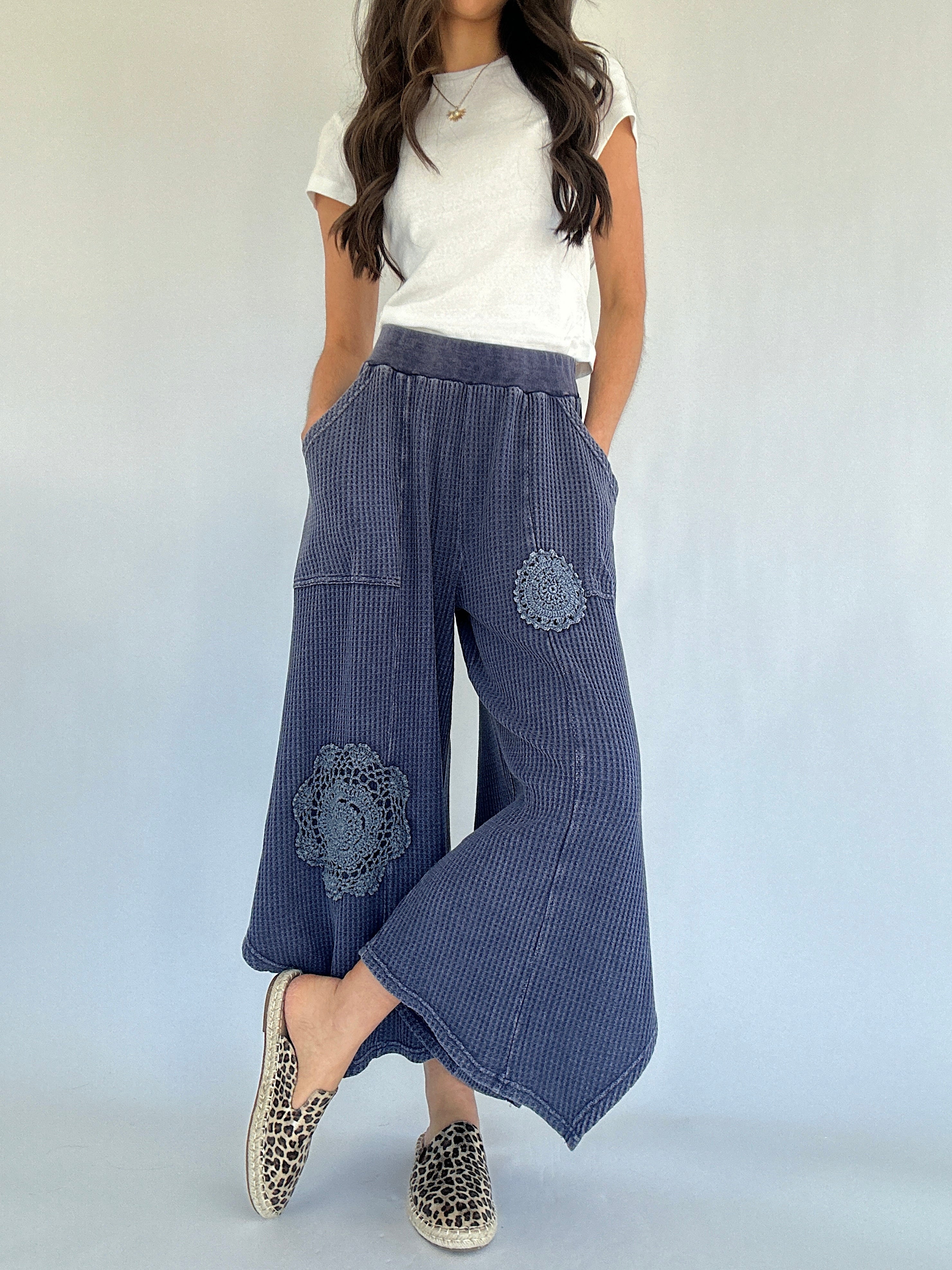 Woman wearing blue waffle knit wide-leg pants with floral crochet embroidery on a white background