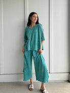 Woman wearing a teal outfit standing against a white wall