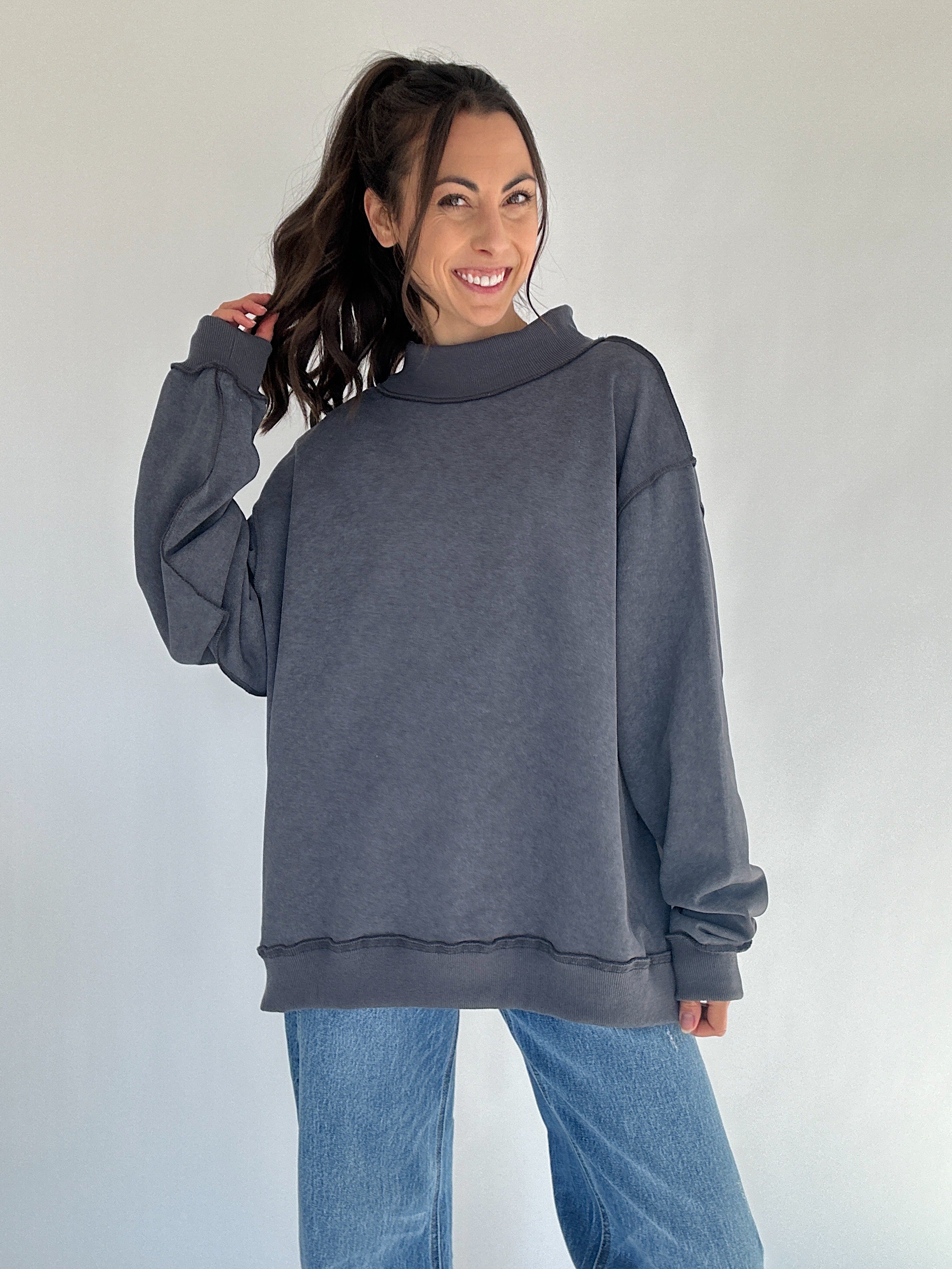 Woman wearing a gray mock neck sweatshirt and blue jeans against a white background