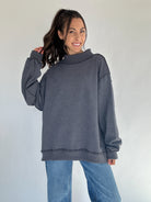 Woman wearing a gray mock neck sweatshirt and blue jeans against a white background