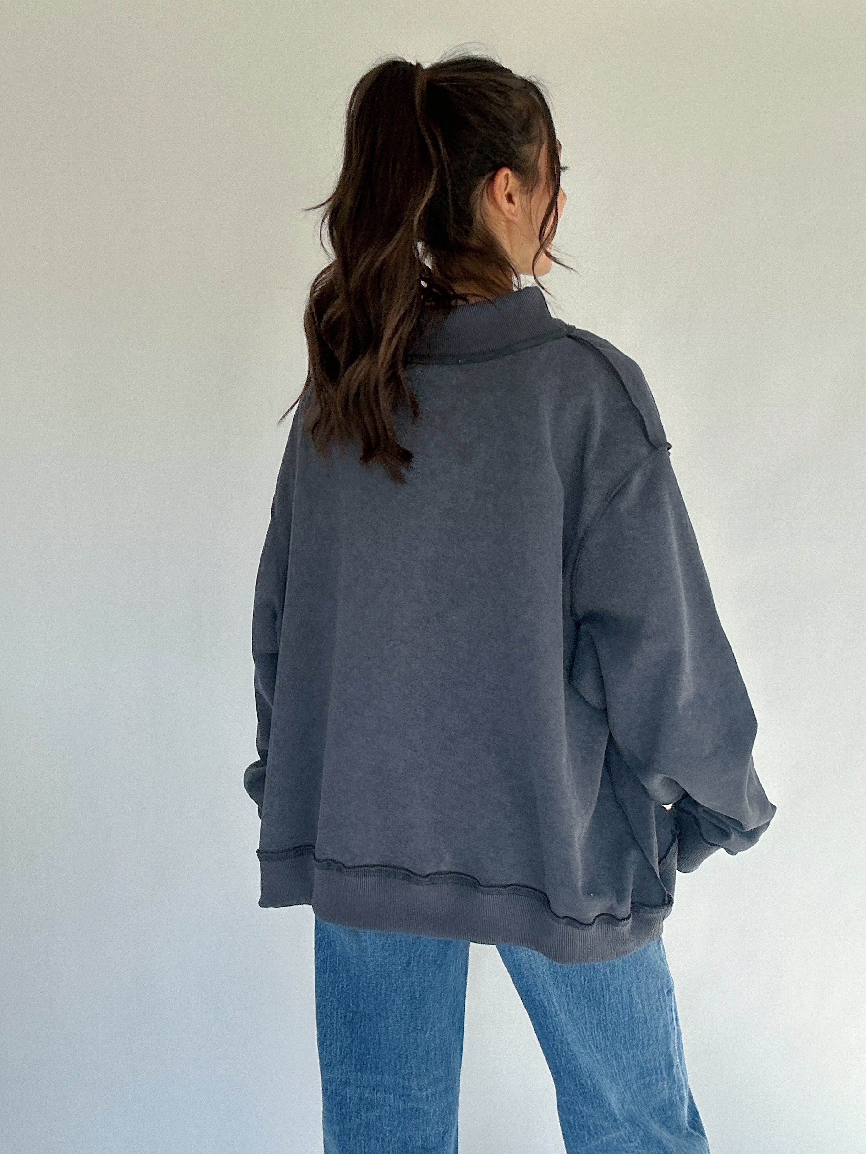 Person wearing a dark gray oversized sweatshirt and blue jeans against a plain background