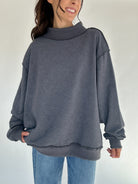 Person wearing a gray oversized mock neck sweatshirt and blue jeans on a plain background