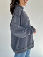 Person wearing a gray oversized sweater against a plain background showing side