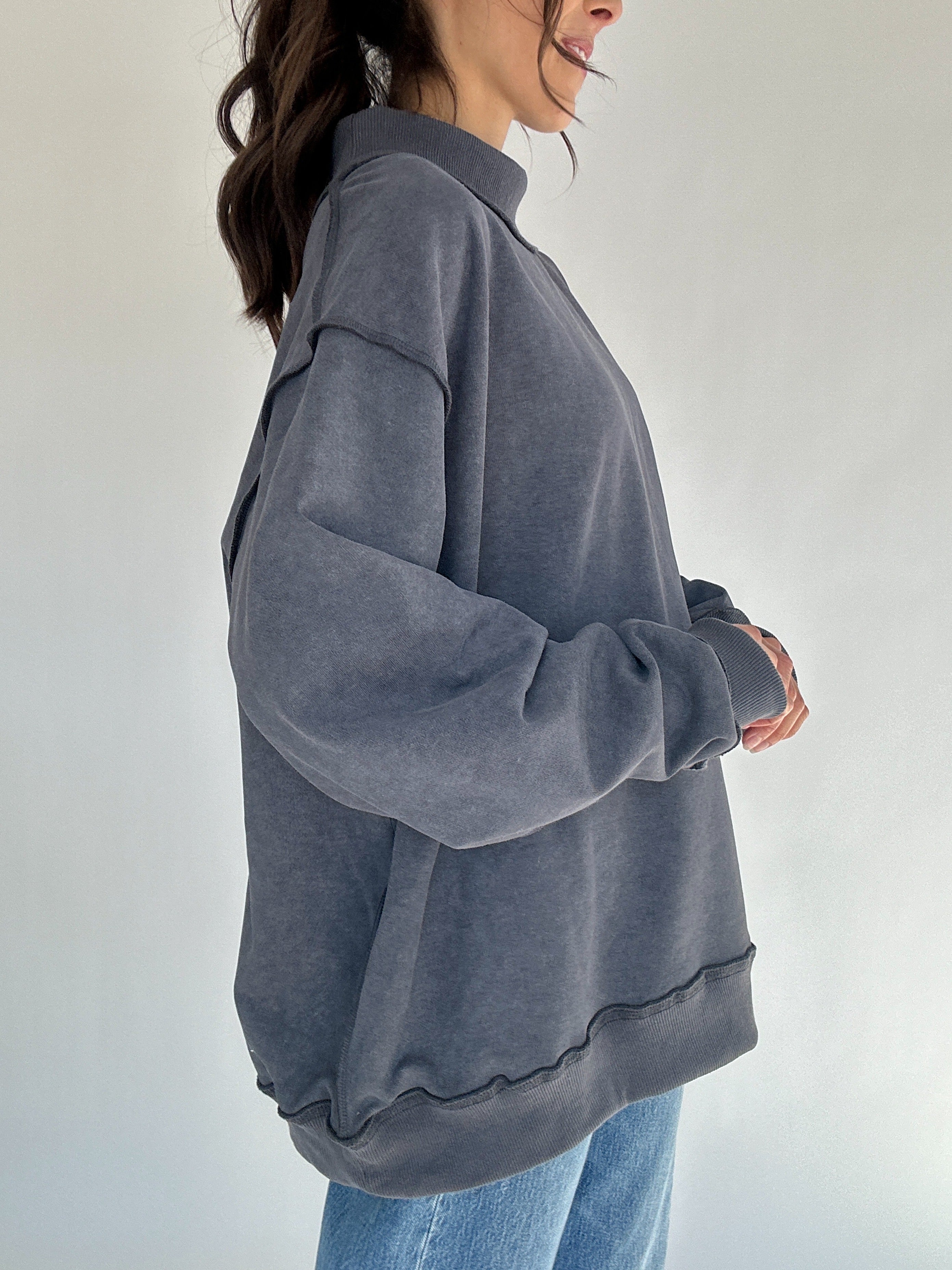 Person wearing a gray oversized sweater against a plain background showing side