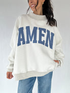 Person wearing a white sweatshirt with 'AMEN' printed in blue on a plain background