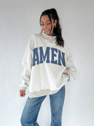 Person wearing a white sweatshirt with 'AMEN' printed in blue on a plain background