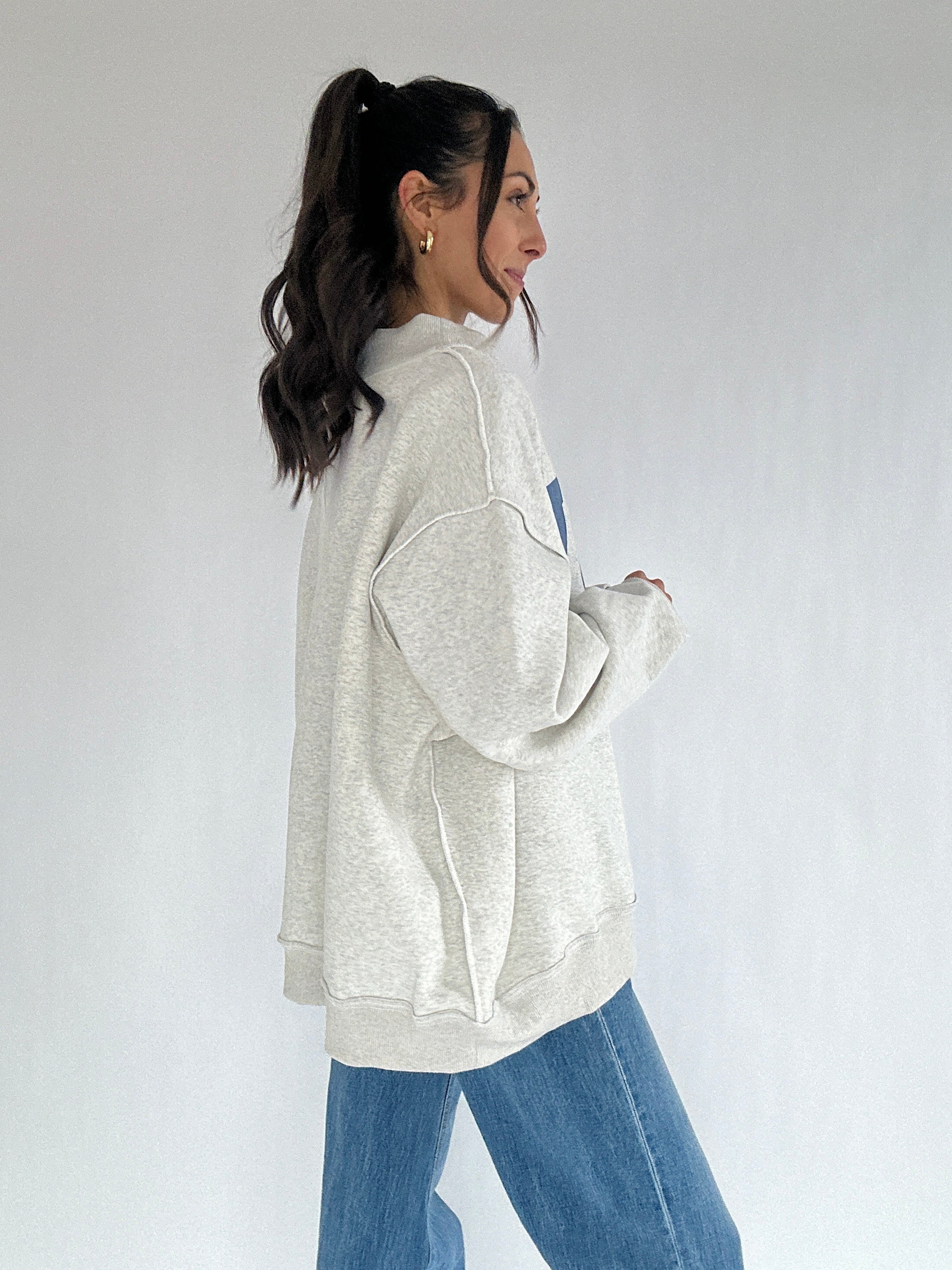 Woman wearing a light gray oversized sweatshirt and blue jeans on a white background from side