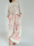 Person wearing a beige sweater with a peace symbol and floral pants on a plain background