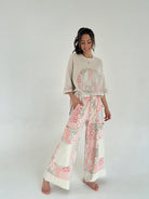 Woman wearing a beige peace sign top and patterned pants on a white background