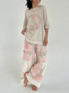 Woman wearing a beige top with a peace symbol and patterned pants on a white background