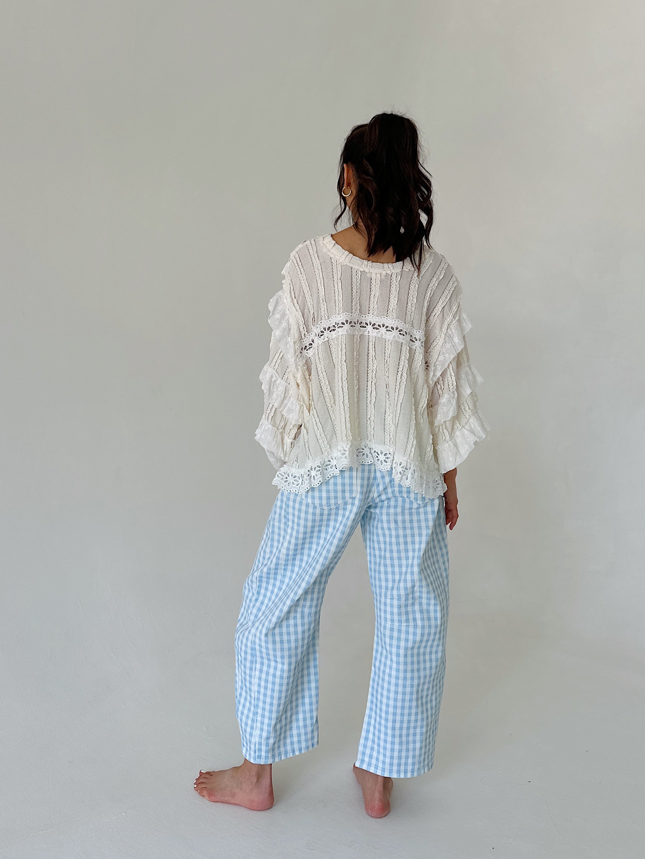 Person wearing a white lace top and blue checkered pants against a plain background