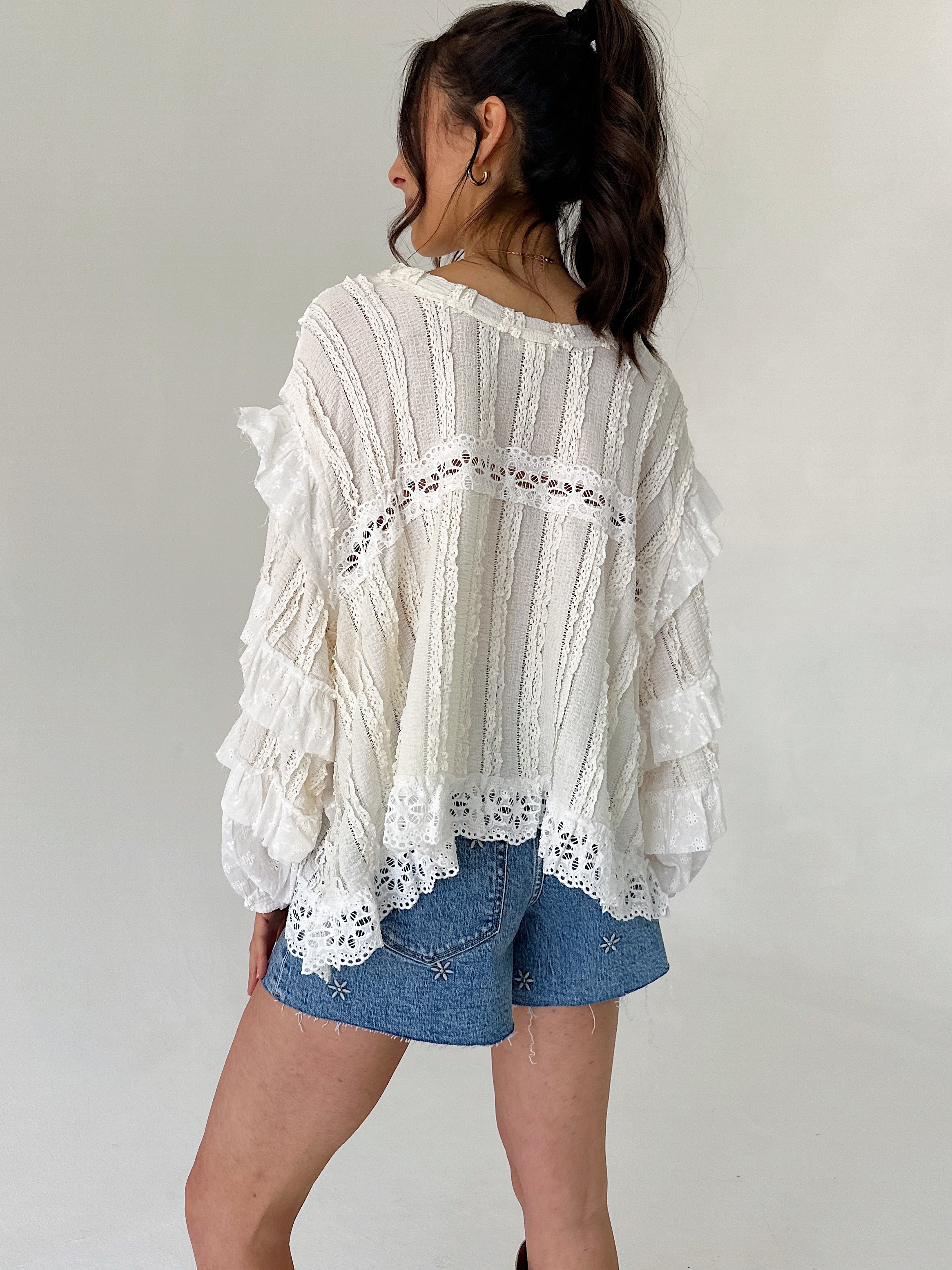 Person wearing a white lace top and denim shorts against a plain background