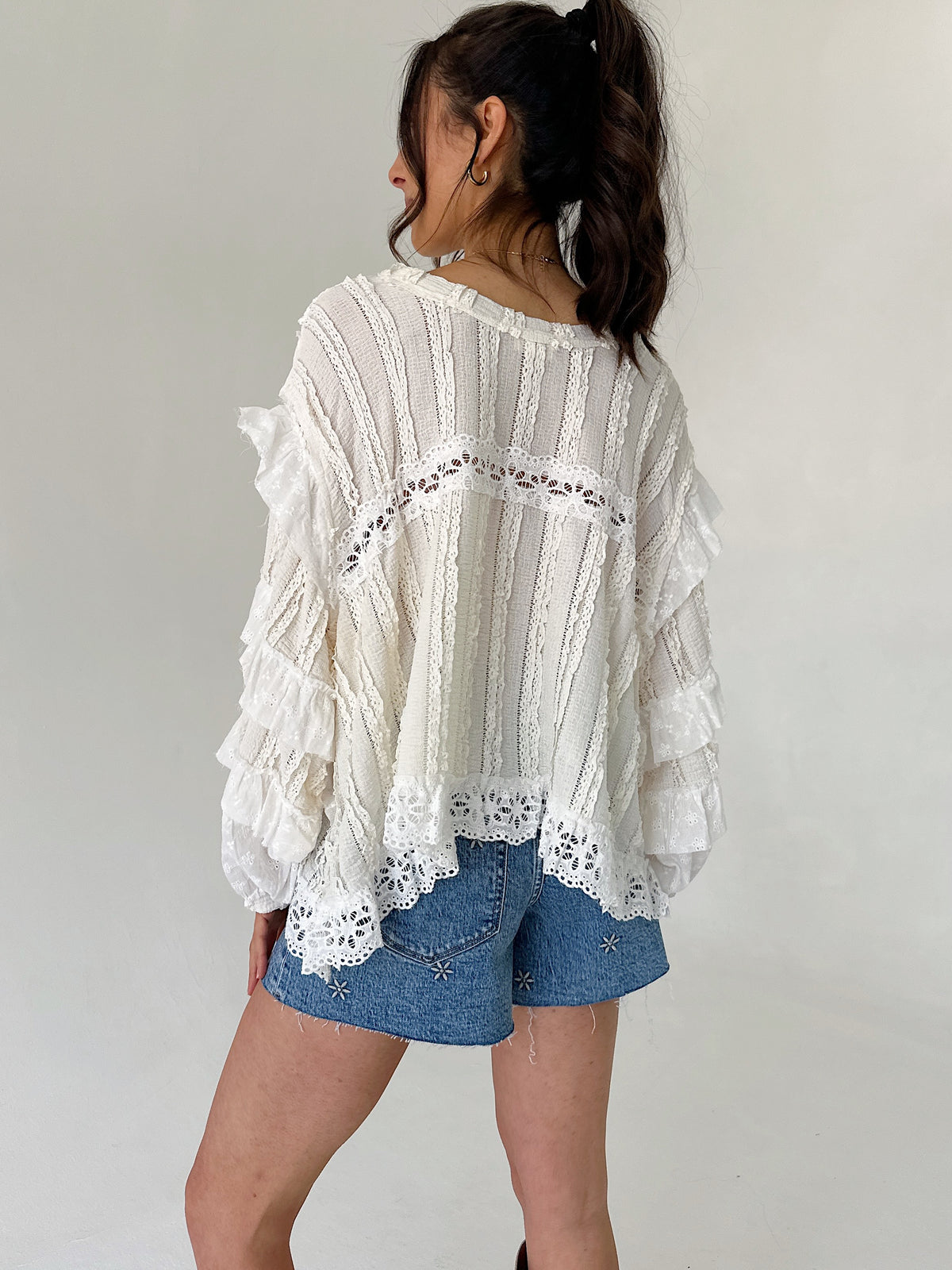 Person wearing a white lace top and denim shorts against a plain background