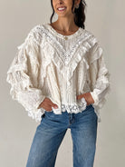 A woman wearing a cream-colored, heavily ruffled and lace-trimmed long-sleeve blouse paired with blue jeans, standing against a plain light gray wall.