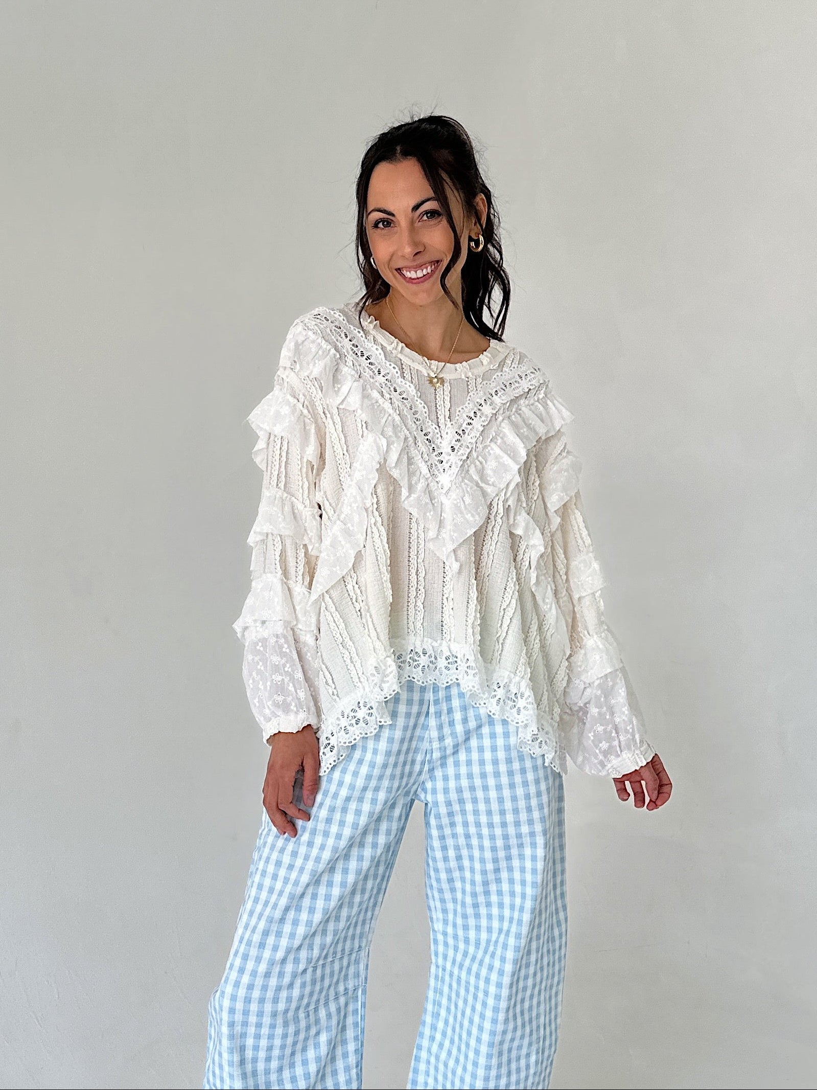 Woman wearing a white lace top and blue checkered pants against a plain background