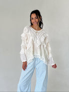 Woman wearing a white lace top and blue checkered pants against a plain background