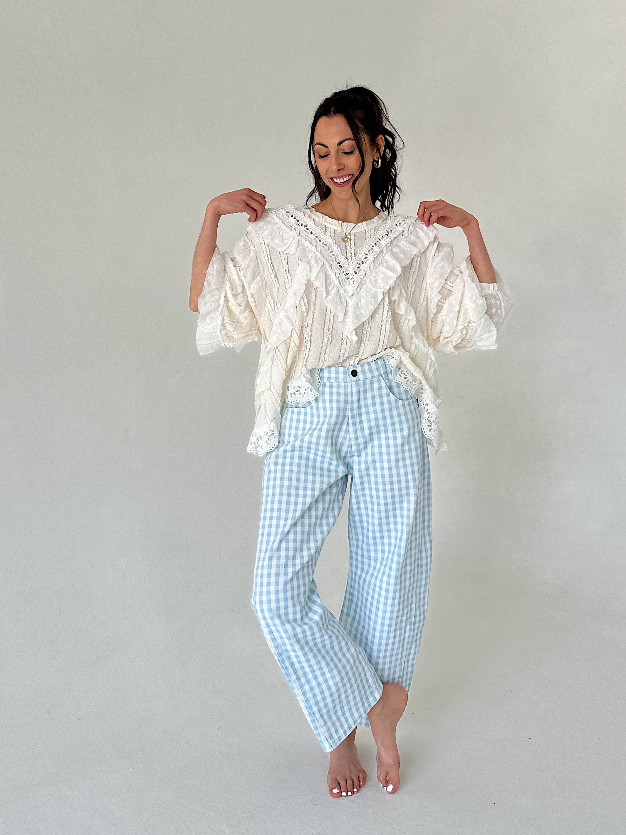 Woman wearing a white lace top and light blue checkered pants against a plain background