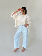 Woman wearing a white lace top and light blue checkered pants against a plain background