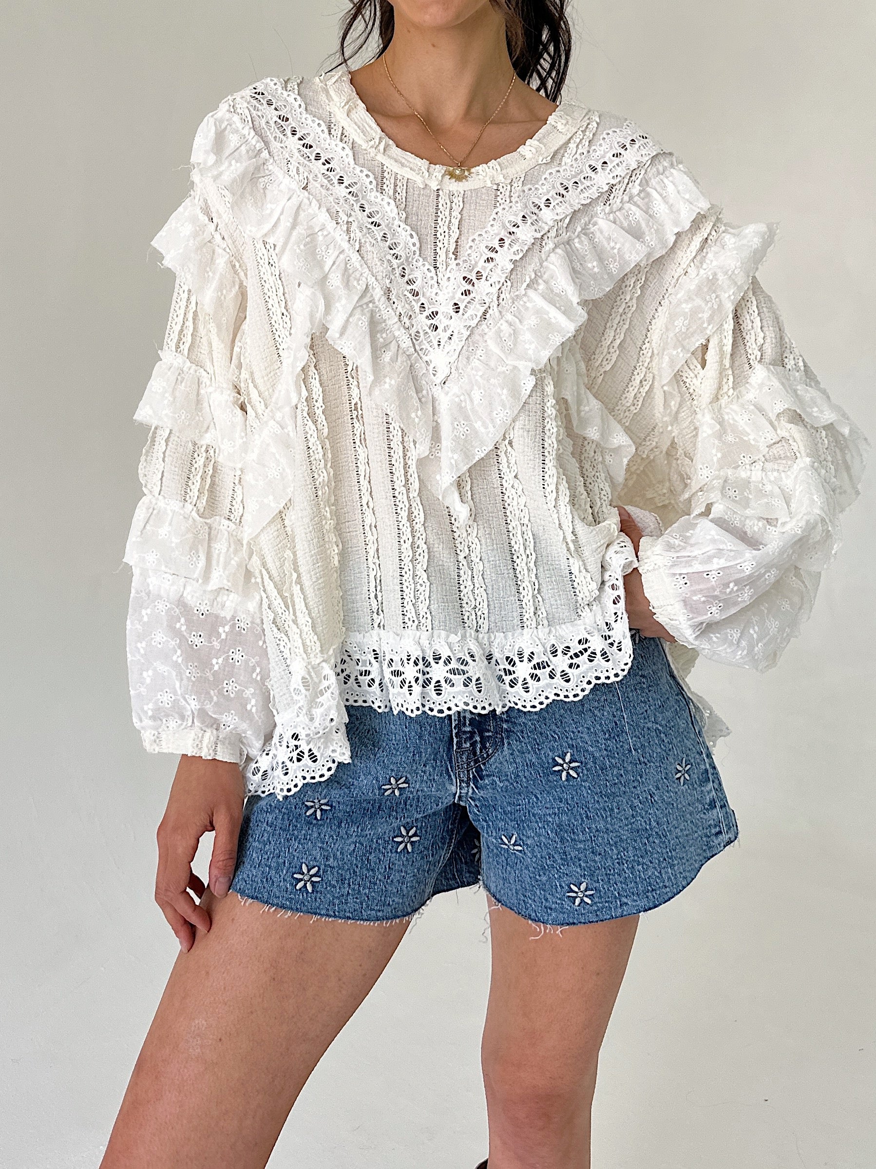 Person wearing a white lace blouse and denim shorts on a plain background