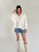 Woman wearing a white lace blouse, denim shorts, and beige knee-high boots against a plain background