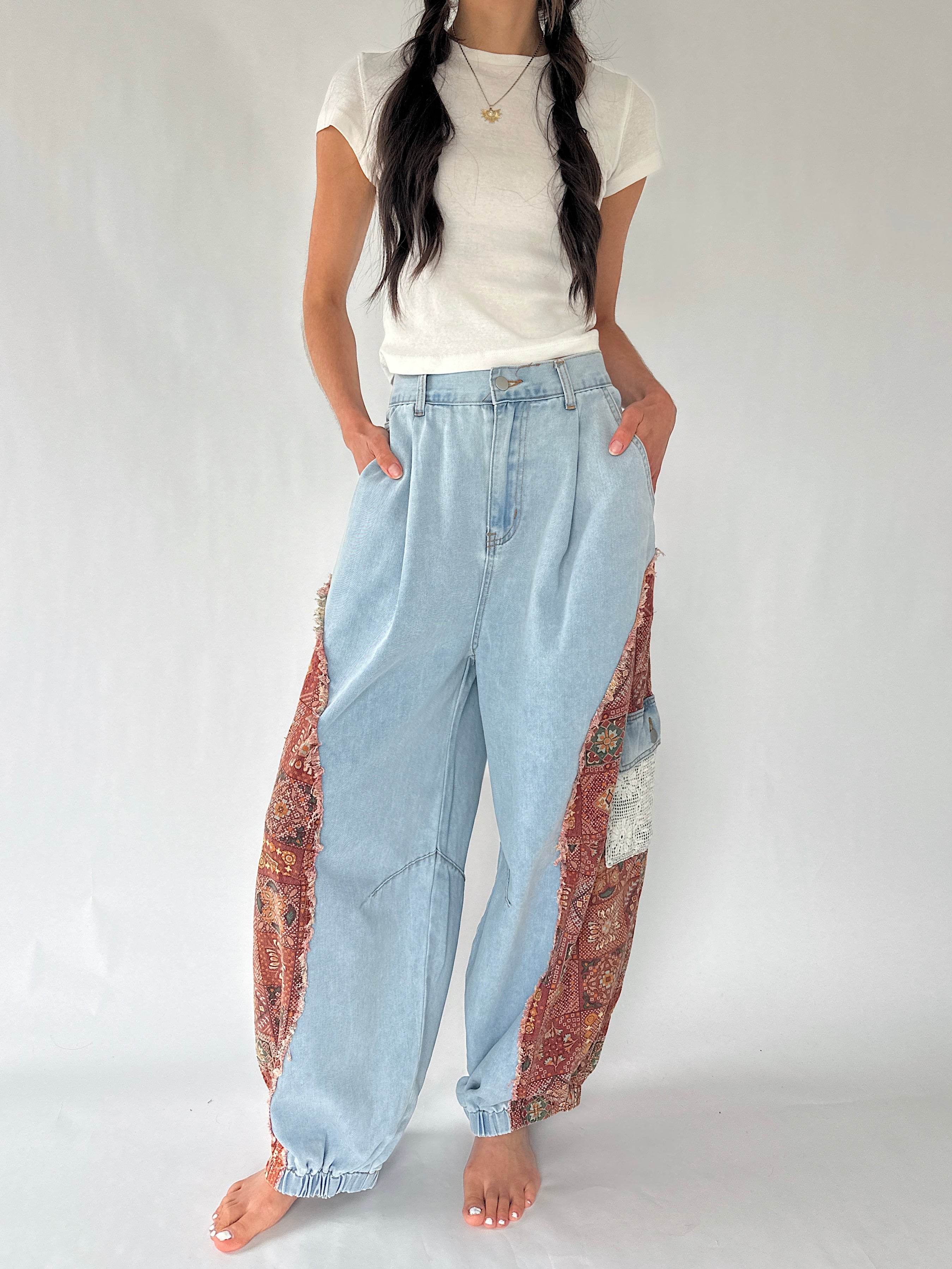 A model wearing light blue wide-leg denim pants with ornate red and gold patterned fabric panels on the outer sides, styled with a white t-shirt against a plain light background.