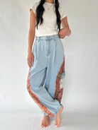 A model wearing light-wash wide-leg denim pants with colorful patterned fabric panels along the sides, paired with a white t-shirt, standing against a plain light background.