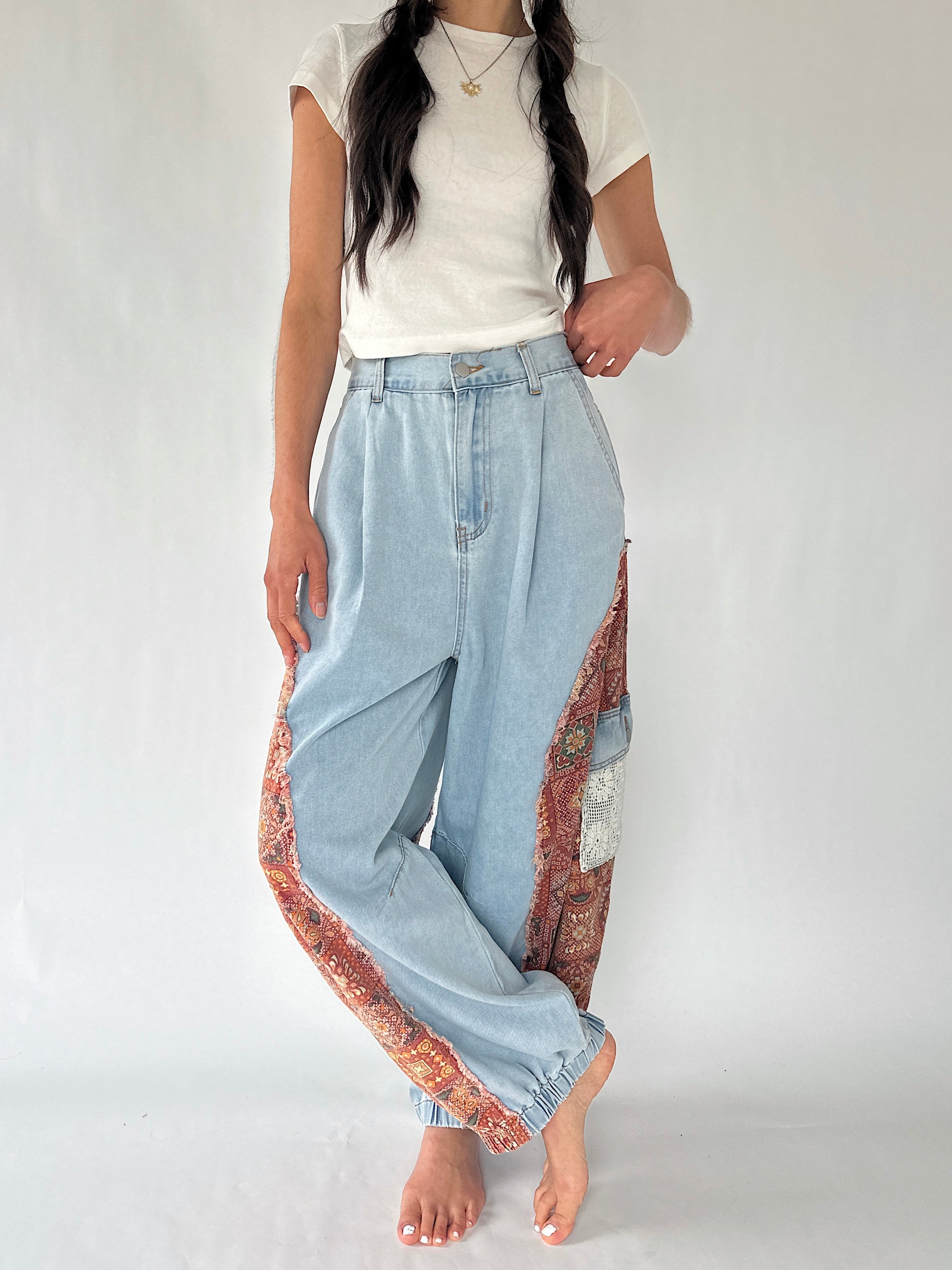 A model wearing light-wash wide-leg denim pants with colorful patterned fabric panels along the sides, paired with a white t-shirt, standing against a plain light background.