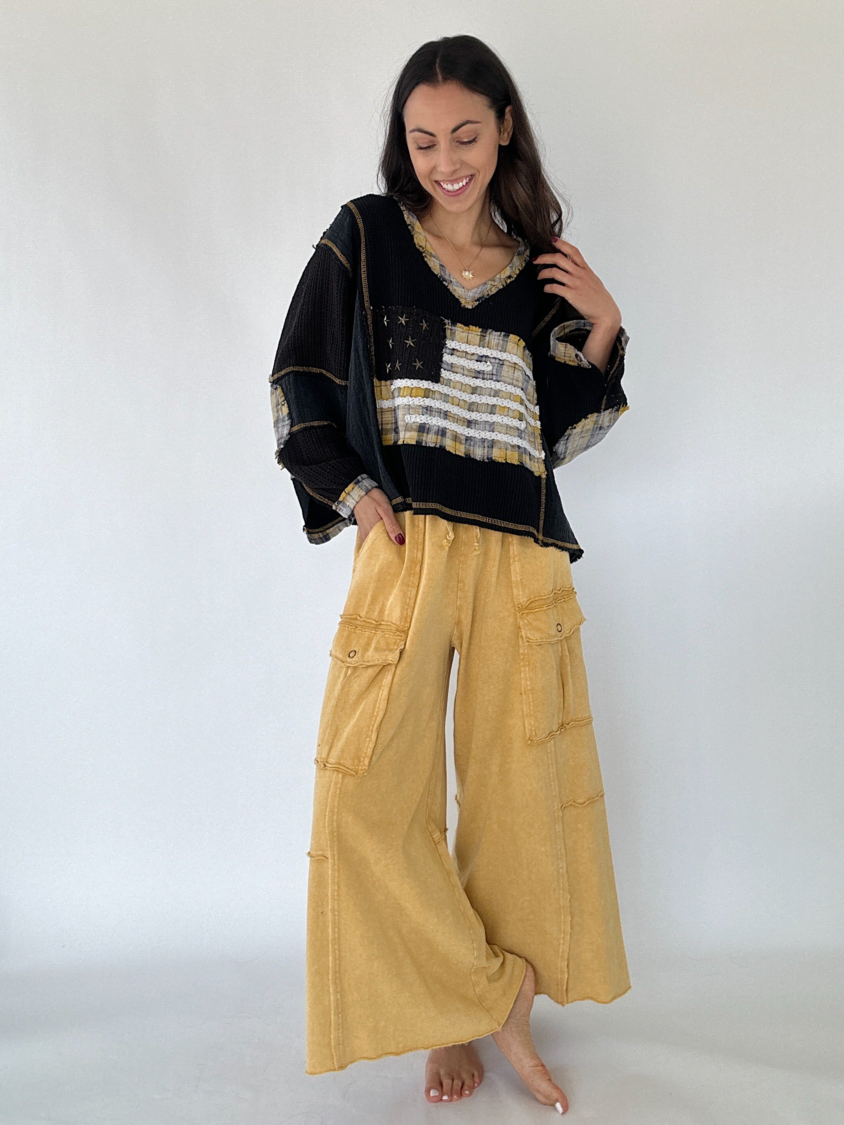 Woman wearing a black top with gold American flag and yellow wide-leg pants on a white background
