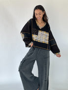 Woman wearing a black and gold patterned sweater with American flag design and with black wahed pants on a white background