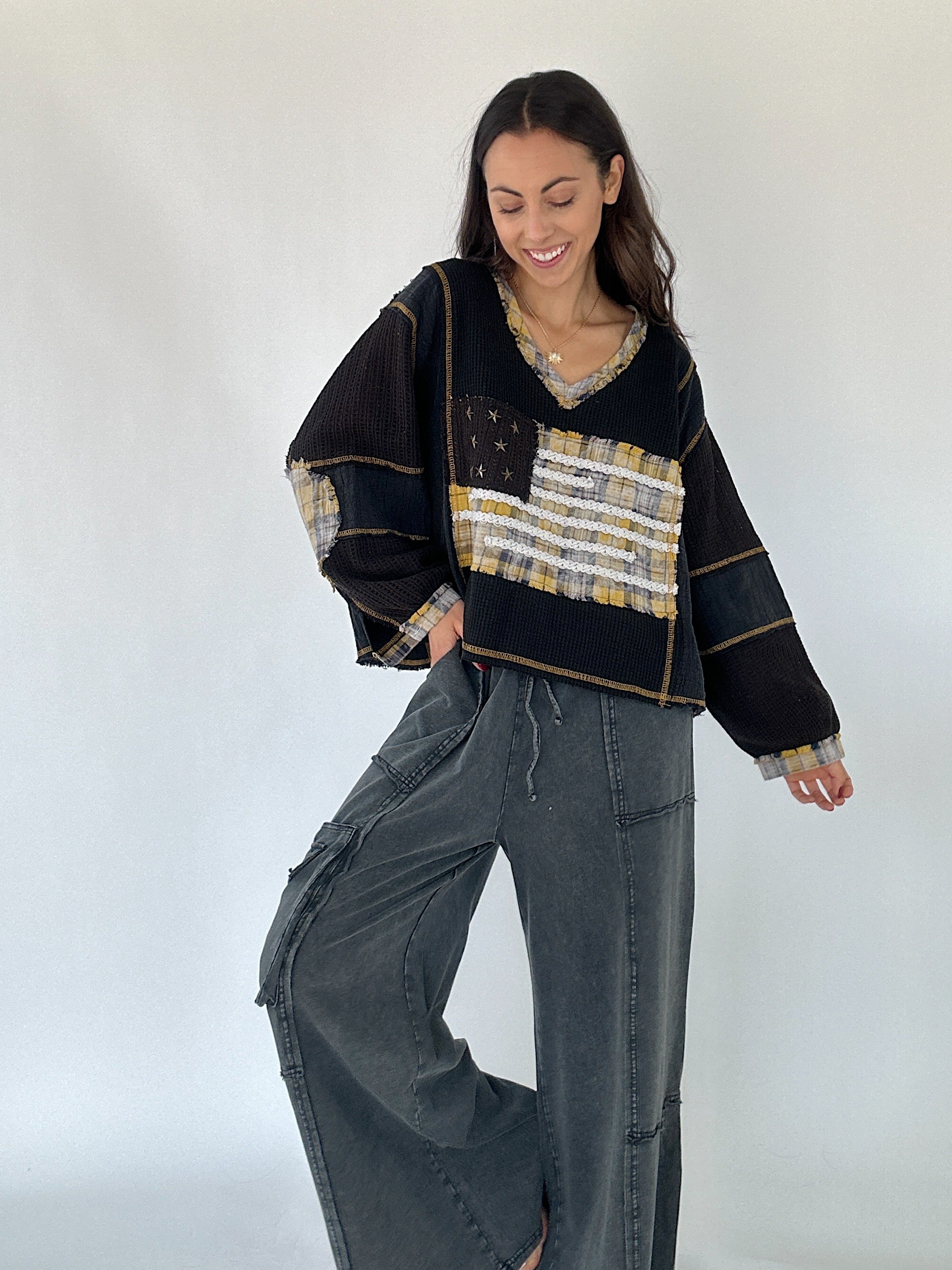 Woman wearing a black and gold patterned sweater with American flag design and with black wahed pants on a white background