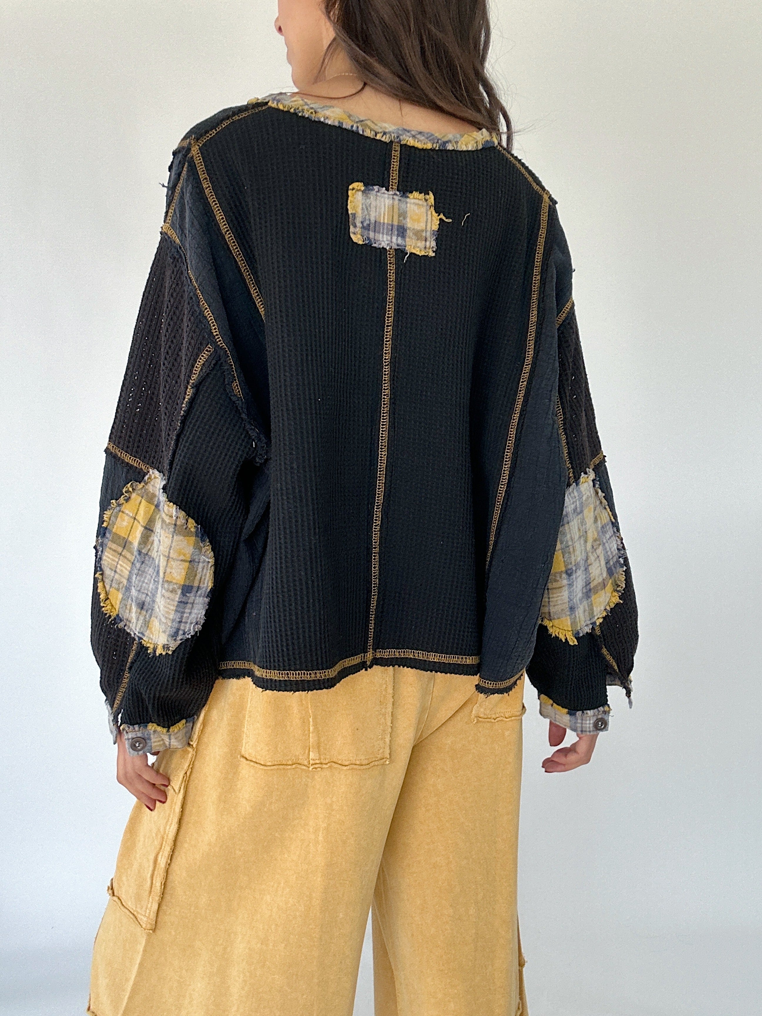 Person wearing a black sweater with plaid patterned elbow patches on a plain background