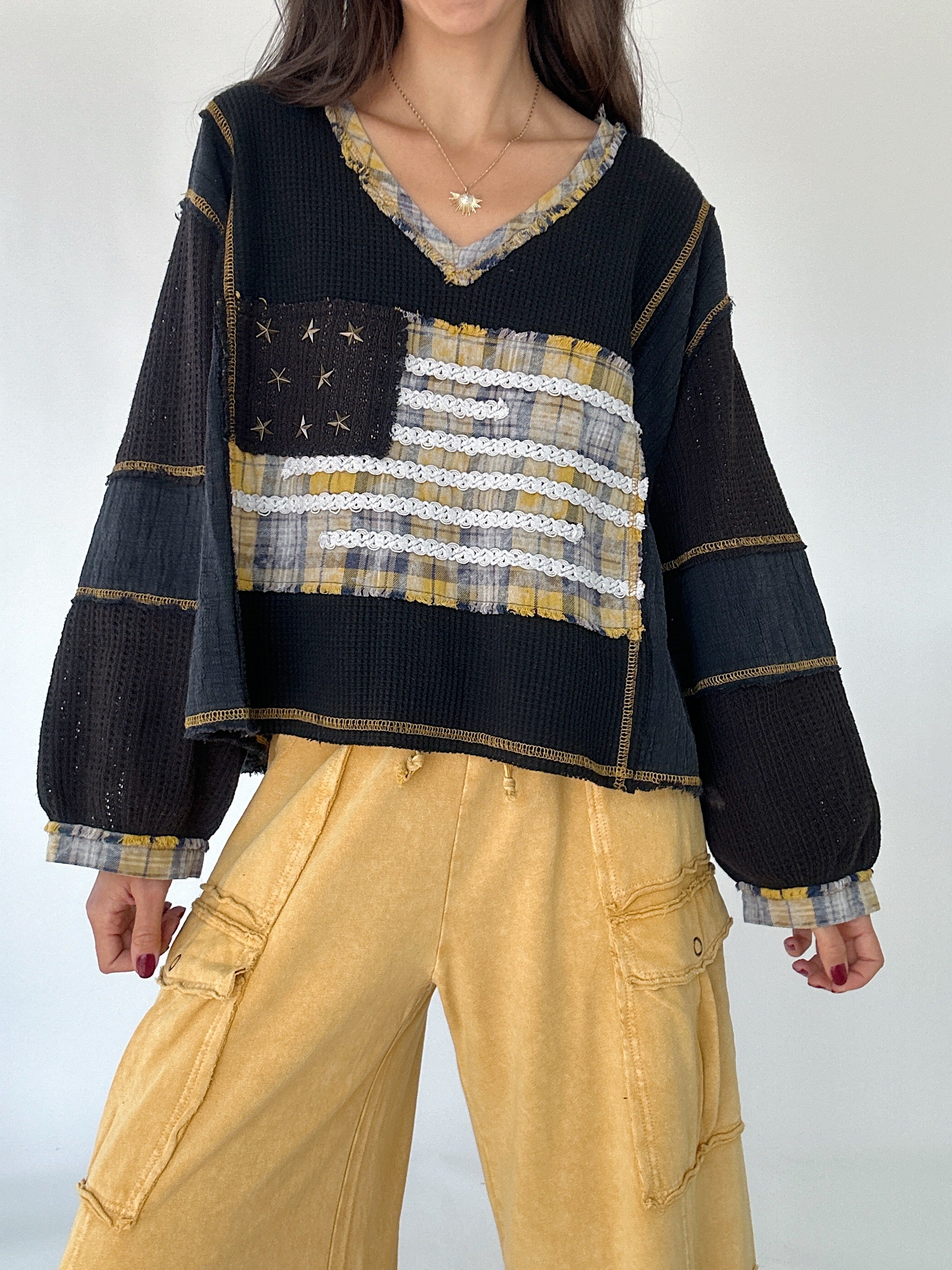 Person wearing a black sweater with a plaid pattern American flag and yellow pants on a white background