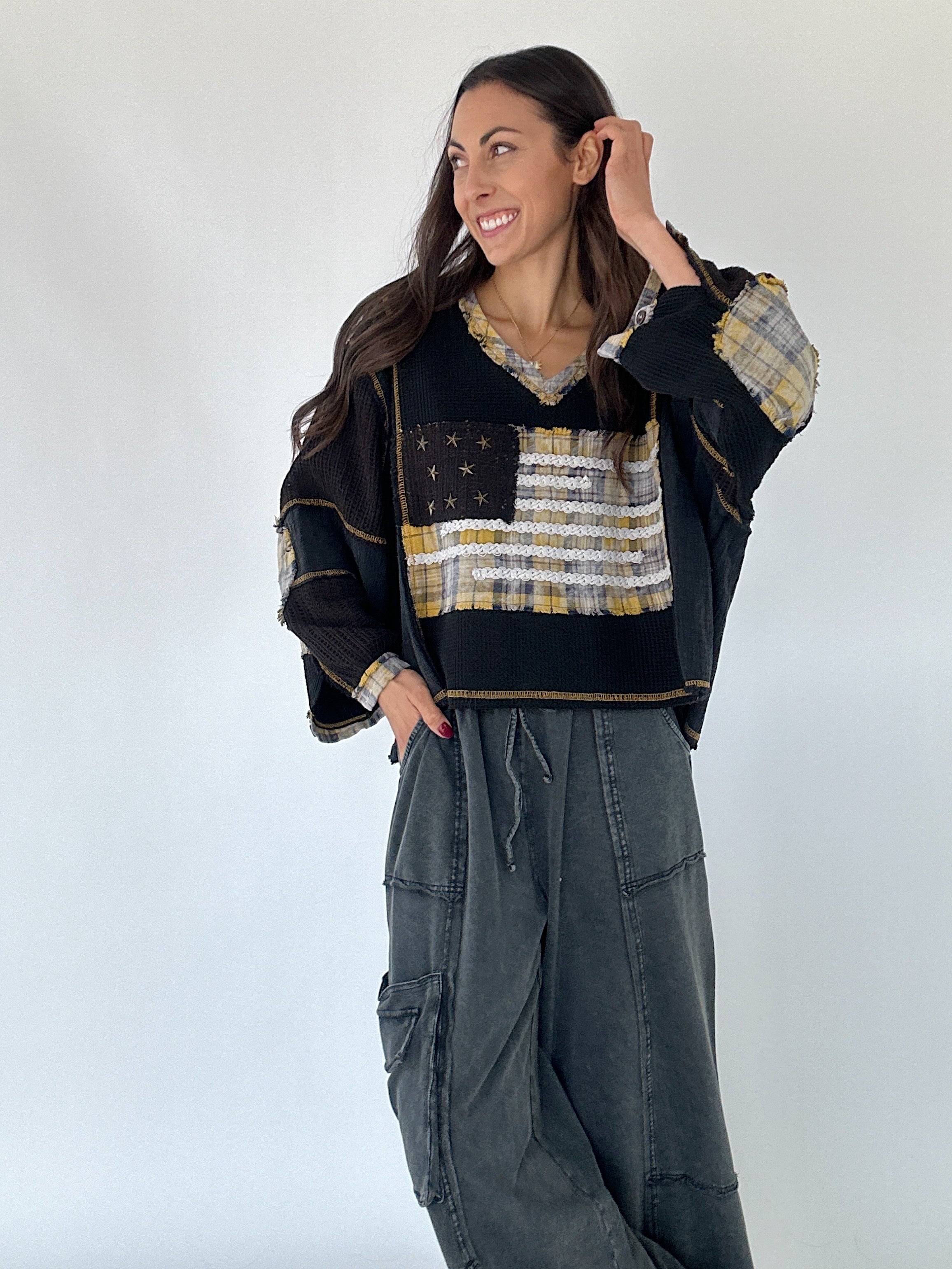 Woman wearing a black top with plaid American flag design and washed black wide leg pants against a white background
