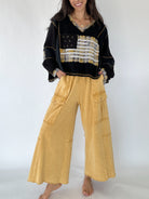 Person wearing a black sweater with a flag design and yellow cargo pants on a white background