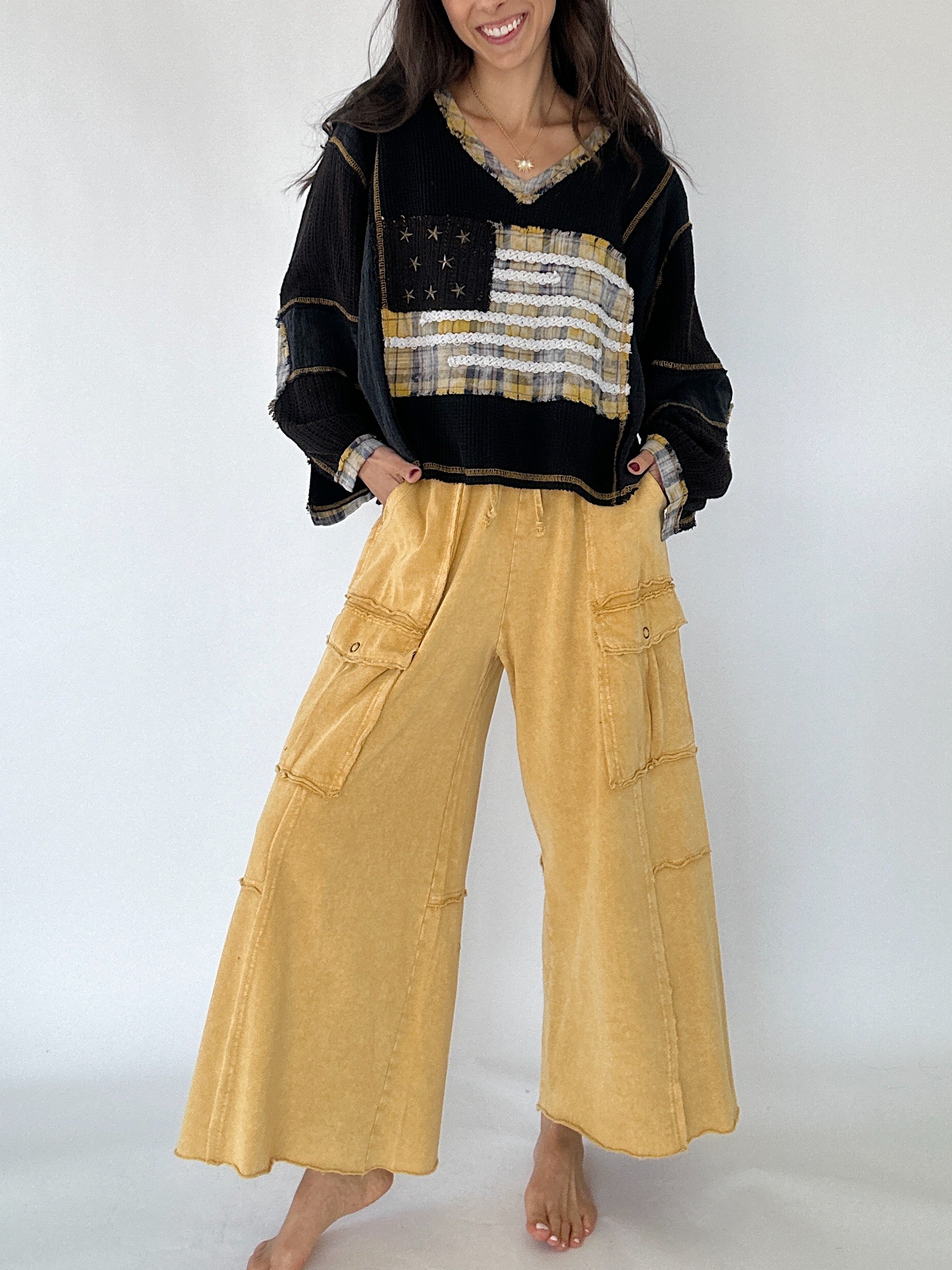 Person wearing a black sweater with a flag design and yellow cargo pants on a white background