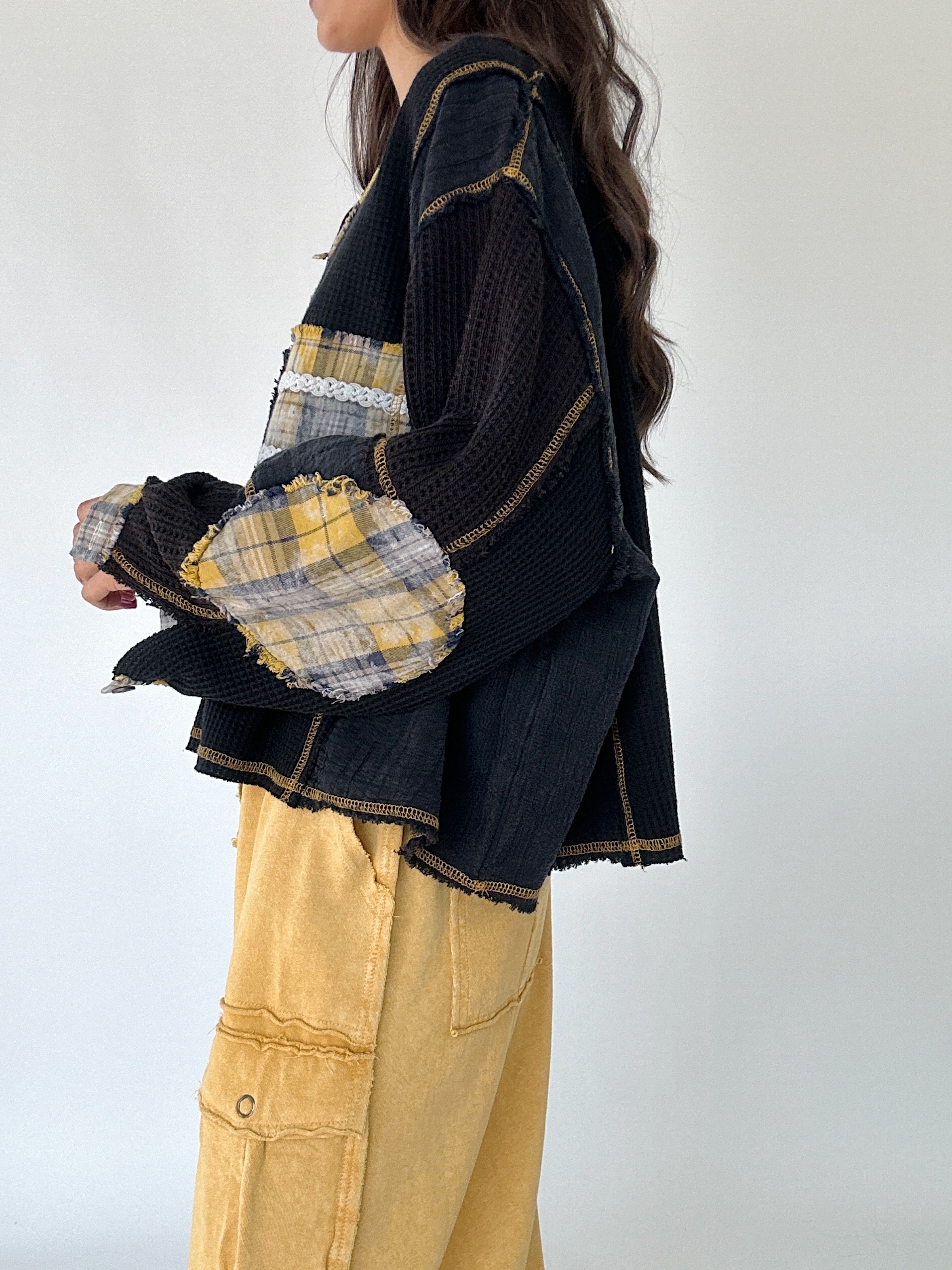 Person wearing a black pullover sweater with yellow plaid accents and mustard pants on a white background