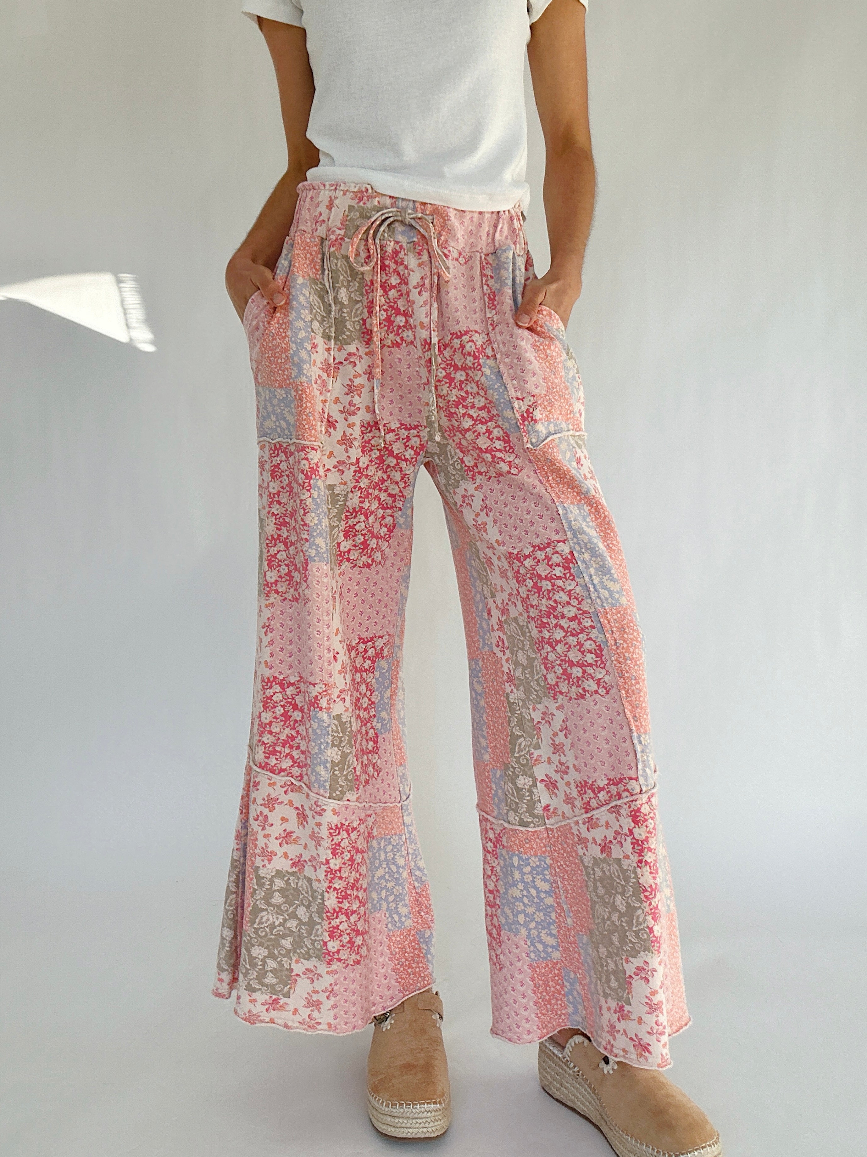 Person wearing floral patchwork pants on a plain background with hands in pockets